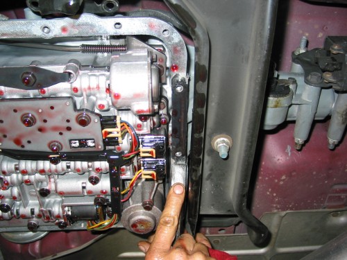 Scrape off any excess gasket material that may have stuck to the tranny or pan.  You can use a putty knife, razor blade, or about anything sharp.  Just be careful that if what you are using is fairly sharp that you don't gouge up and mar the sealing surface with your scraper.
